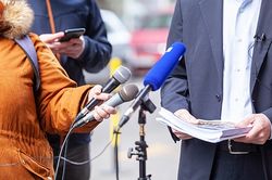 Foto: Interviewsituation, im Vordergrund Mikrofone, dahinter Interviewter im Anzug mit Dokumenten in den Händen © wellphoto/stock.adobe.com