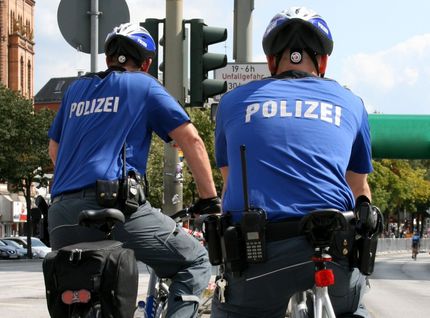 Rückenansichten zweier Polizisten auf Fahrrädern in Sommer-Uniform.