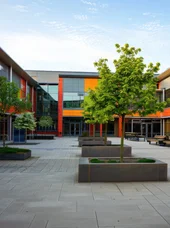 Zertifikatslehrgang "Fachkraft Schulbauplanung" Dieses Bild zeigt Schulhof und modernes Schulgebäude mit bunten Fassadenelementen.