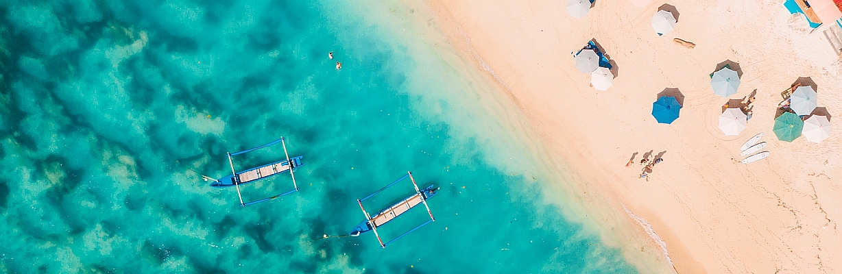 Luftbildaufnahme eines Strandes in Indonesien mit Booten auf türkisfarbenem Wasser. 